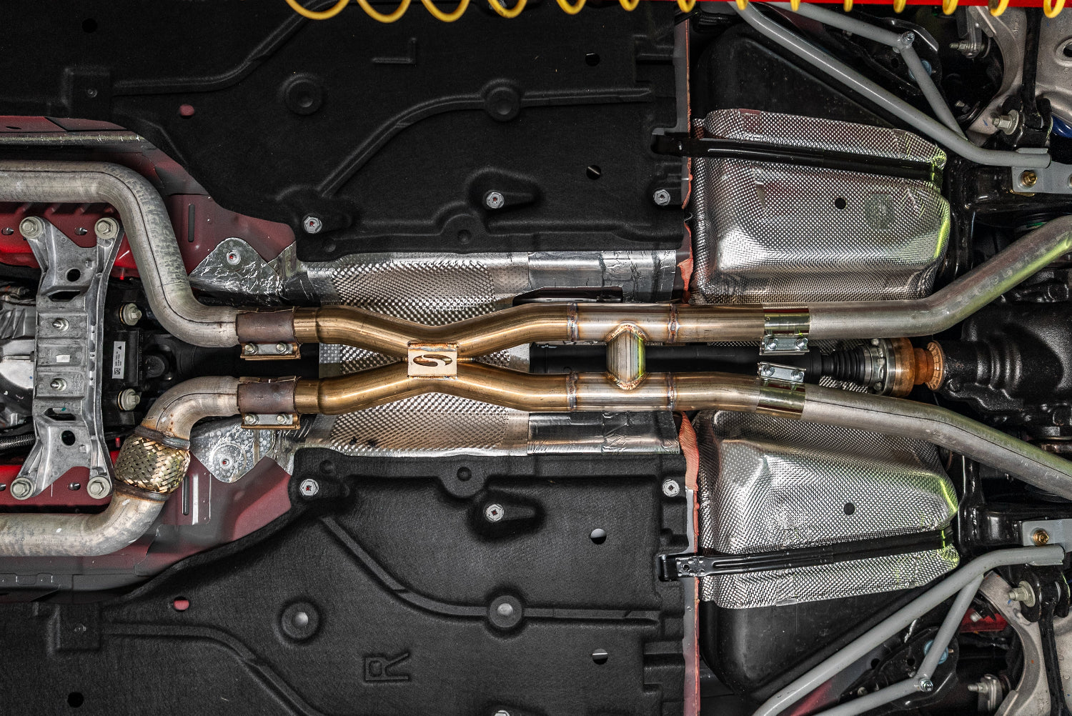 Close-up of a Mustang exhaust system with metallic X and H pipes and components.